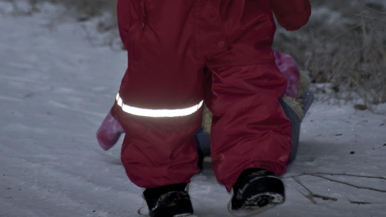 Barn i vinteroverall med reflex som går i snön i mörkret.
