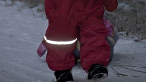 Barn i vinteroverall med reflex som går i snön i mörkret.